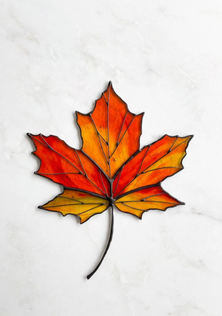 DIY stained glass maple leaf craft with translucent red and orange sections and black outlines, a vibrant idea for fall crafts for kids.   
