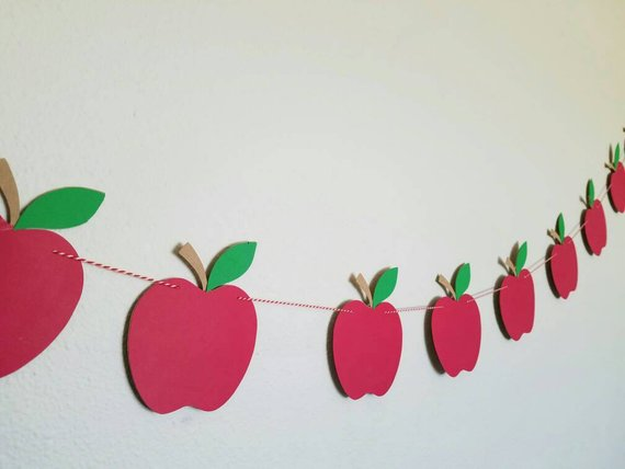 Red paper apple garland strung on twine hanging on a wall, an easy classroom idea for fall crafts for kids.   
