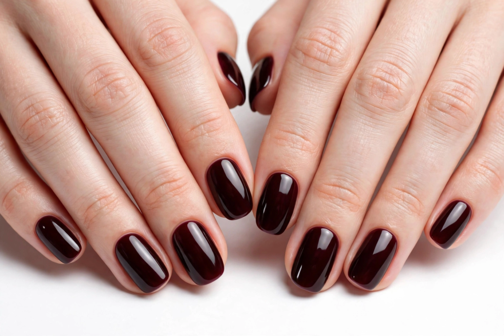 October nail ideas 2026 showing a glossy deep burgundy and dark wine red manicure on short, squoval-shaped nails against a clean white background.   