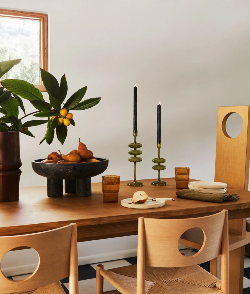 Modern fall decor ideas for a dining table featuring a pedestaled fruit bowl filled with bosc pears, green glass taper candle holders with black candles, and amber ribbed glasses.   
