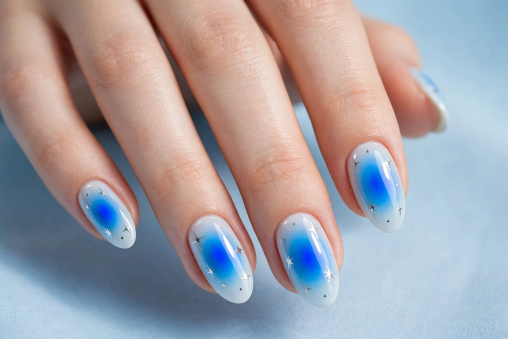 Celestial blue aura nails with milky white base, vibrant royal blue airbrushed centers, and silver star accents for 2026 nail art trends.   