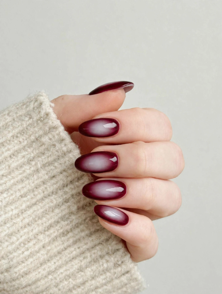 Burgundy aura nails featuring glossy oval tips with deep wine-red edges framing a diffused milky white center, trending for fall and winter 2026 nail designs.   