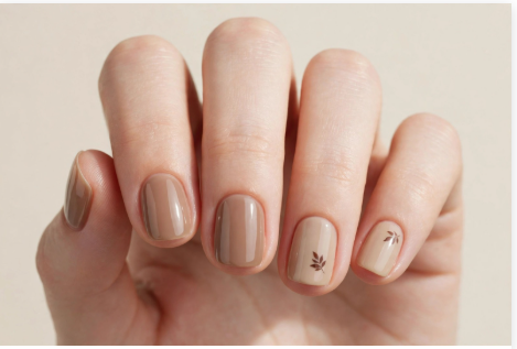 Short squoval fall October nails 2026 featuring a tonal neutral taupe and light beige manicure accented with delicate hand-painted brown autumn leaf silhouettes.